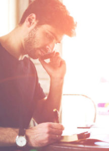 man writing in journal and on the phone